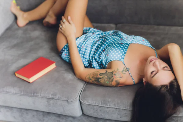 잠옷을 입고 소파에서 책을 읽고 있는 아름다운 여성. — 스톡 사진