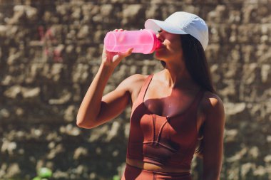 Yüzeysel bir göbek ve ince bir kadın, bir şişe su tutuyor ve bileklik takıyor. Şehirde sabah seansı. Üzerine dökülüyor.