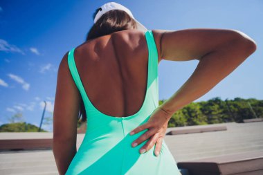 Sırt ağrısı. Pembe spor giysili atletik bir kadın, deniz kenarında dikiliyor, sırt kaslarını ovuyor, gövdesini kesiyor..