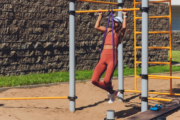 Motivierte, konzentrierte athletische Frau, die Sport treibt, trainiert, mit Gummistreifen trainiert, elastisches Seil für Muskeldehnung und Krafttraining verwendet. — Stockfoto