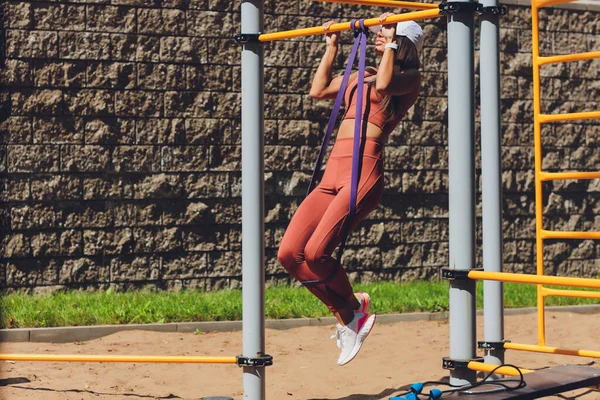 Motivierte, konzentrierte athletische Frau, die Sport treibt, trainiert, mit Gummistreifen trainiert, elastisches Seil für Muskeldehnung und Krafttraining verwendet. — Stockfoto