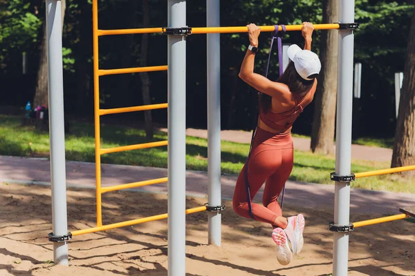 Mulher atlética motivada e concentrada fazendo esportes, treinando, exercitando com faixa de expansor de borracha, usando corda elástica para alongamento muscular e exercícios de força. — Fotografia de Stock