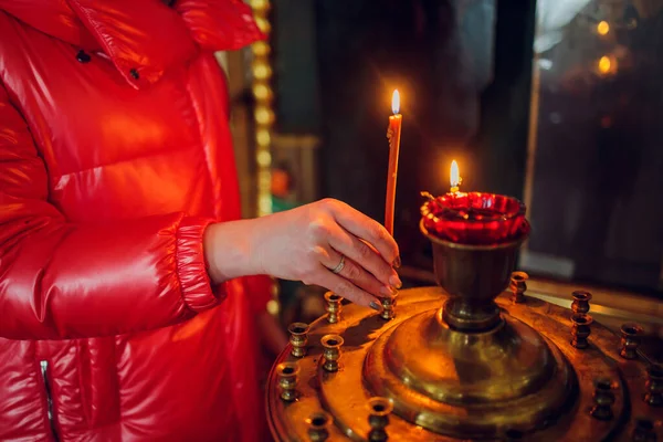 Mão de mulheres em uma jaqueta vermelha põe uma vela de igreja. — Fotografia de Stock