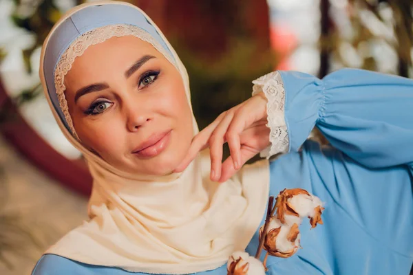 Joven hermosa mujer caucásica con el tradicional pañuelo musulmán en la cafetería hipster con grandes ventanas de cuerpo entero. Mujer en hijab azul en acogedora cafetería. Fondo, espacio de copia, primer plano retrato. —  Fotos de Stock