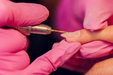 Bir kadın kuaförde manikür yapıyor, usta çalışırken tırnaklarını kesiyor, manikür yapıyor. Eldivenli eller.