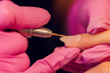 Bir kadın kuaförde manikür yapıyor, usta çalışırken tırnaklarını kesiyor, manikür yapıyor. Eldivenli eller.