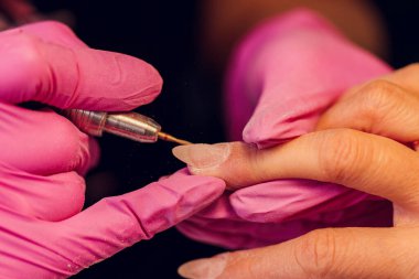 Bir kadın kuaförde manikür yapıyor, usta çalışırken tırnaklarını kesiyor, manikür yapıyor. Eldivenli eller.