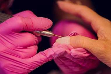 Bir kadın kuaförde manikür yapıyor, usta çalışırken tırnaklarını kesiyor, manikür yapıyor. Eldivenli eller.