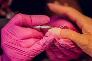 Bir kadın kuaförde manikür yapıyor, usta çalışırken tırnaklarını kesiyor, manikür yapıyor. Eldivenli eller.