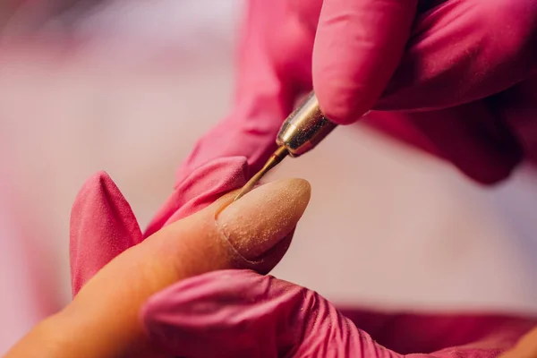 Una mujer hace manicura con un dispositivo de uñas en un salón de belleza, el maestro se corta las uñas, manicura mientras trabaja. Manos con guantes. —  Fotos de Stock