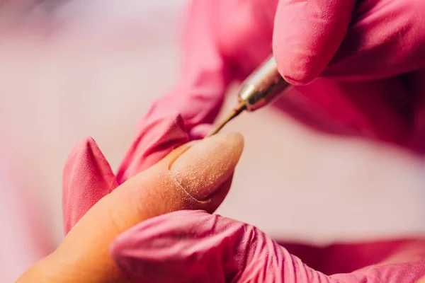 Una mujer hace manicura con un dispositivo de uñas en un salón de belleza, el maestro se corta las uñas, manicura mientras trabaja. Manos con guantes. —  Fotos de Stock