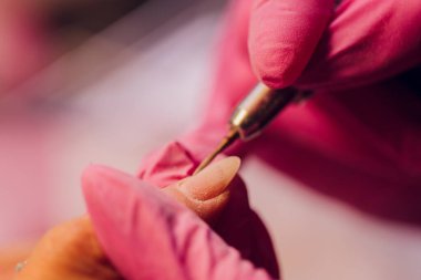 Bir kadın kuaförde manikür yapıyor, usta çalışırken tırnaklarını kesiyor, manikür yapıyor. Eldivenli eller.