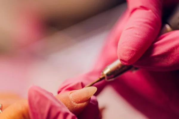 Una mujer hace manicura con un dispositivo de uñas en un salón de belleza, el maestro se corta las uñas, manicura mientras trabaja. Manos con guantes. —  Fotos de Stock