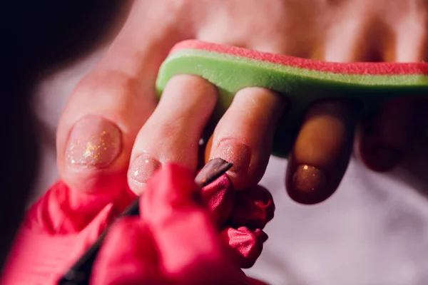 Τα χέρια στα γάντια νοιάζονται για τα νύχια ποδιών μιας γυναίκας. Πεντικιούρ, μανικιούρ έννοια σαλόνι ομορφιάς. Βερνίκι νυχιών σε κόκκινο χρώμα. — Φωτογραφία Αρχείου