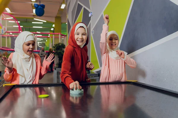 Kinder in muslimischer Kleidung spielen Airhockey. — Stockfoto