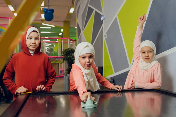 Kinder in muslimischer Kleidung spielen Airhockey. — Stockfoto