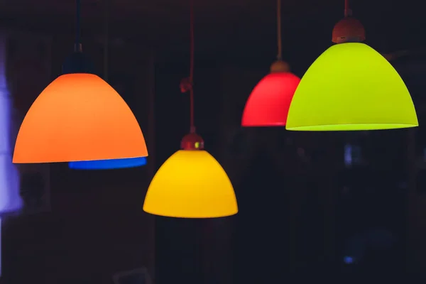 Színes lámpaernyők lógnak sötét háttérrel. A többszínű csillárok összetétele a belső kialakításban. — Stock Fotó
