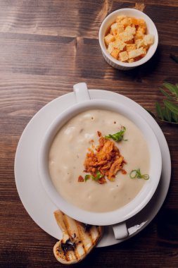 Beyaz tencerelerde mantar çorbası, peçete, ahşap zemin.