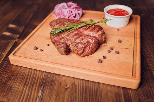 Beef steak with twig rosemary on a wooden table.