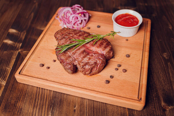 Beef steak with twig rosemary on a wooden table.