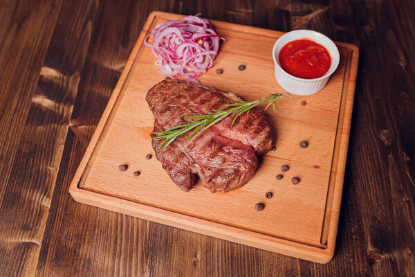 Beef steak with twig rosemary on a wooden table.