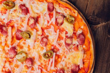 Tahta bir tabakta pizza sosisi, salam ve peynir dilimlerine ayrılmış..