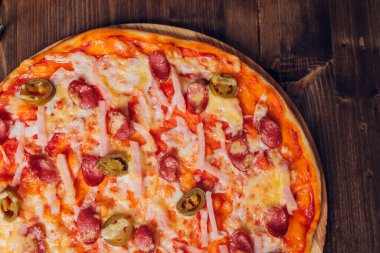 Tahta bir tabakta pizza sosisi, salam ve peynir dilimlerine ayrılmış..