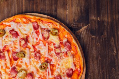 Tahta bir tabakta pizza sosisi, salam ve peynir dilimlerine ayrılmış..