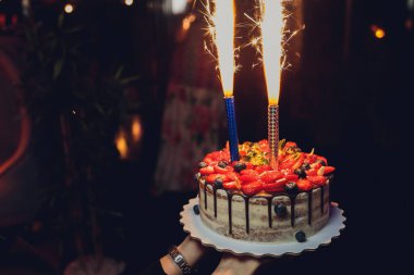 Mumlu doğum günü pastası. Pastadaki mumlar. Tatil için pasta. Koyu arkaplanlı çilekli güzel beyaz pasta. Dikey fotoğraf.