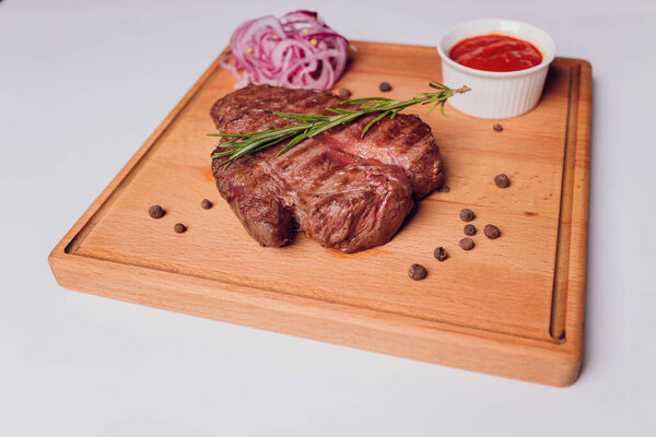 Large meat steak on the bone, grilled, served with grilled vegetables, corn, red onion, sweet peppers, potatoes. Modern serving dishes in the restaurant on a black slate blackboard.