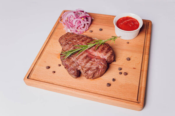 Large meat steak on the bone, grilled, served with grilled vegetables, corn, red onion, sweet peppers, potatoes. Modern serving dishes in the restaurant on a black slate blackboard.