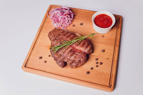 Large meat steak on the bone, grilled, served with grilled vegetables, corn, red onion, sweet peppers, potatoes. Modern serving dishes in the restaurant on a black slate blackboard.