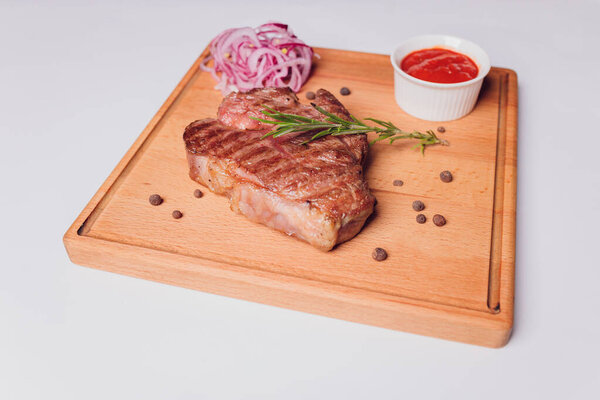 Large meat steak on the bone, grilled, served with grilled vegetables, corn, red onion, sweet peppers, potatoes. Modern serving dishes in the restaurant on a black slate blackboard.