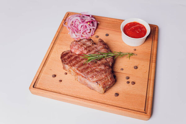 Large meat steak on the bone, grilled, served with grilled vegetables, corn, red onion, sweet peppers, potatoes. Modern serving dishes in the restaurant on a black slate blackboard.