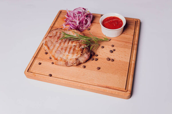 Large meat steak on the bone, grilled, served with grilled vegetables, corn, red onion, sweet peppers, potatoes. Modern serving dishes in the restaurant on a black slate blackboard.