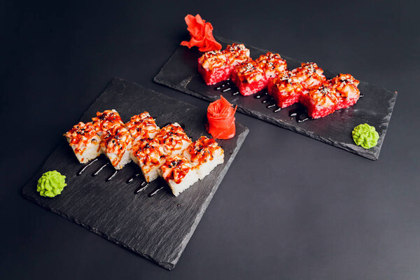 Традиционная еда - смесь разноцветных суши-роллов с лососем, креветками и овощами. На черном деревенском фоне. Вид сверху.