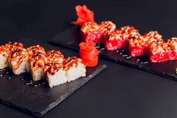 Традиционная еда - смесь разноцветных суши-роллов с лососем, креветками и овощами. На черном деревенском фоне. Вид сверху.