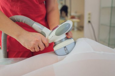 Beyaz takım elbiseli bir kadın spa salonunda selülit karşıtı masaj yaptırıyor. Klinikte LPG ve vücut şekillendirme tedavisi.
