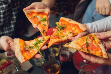 Yemek yemek. İnsanların ellerinin biberli pizzadan dilimler aldığı yakın çekim. Arkadaş gurubu pizzayı paylaşıyor. Fast food, arkadaşlık, eğlence, yaşam tarzı..