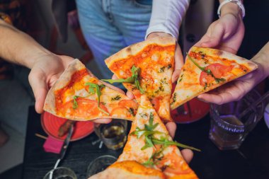 Yemek yemek. İnsanların ellerinin biberli pizzadan dilimler aldığı yakın çekim. Arkadaş gurubu pizzayı paylaşıyor. Fast food, arkadaşlık, eğlence, yaşam tarzı..