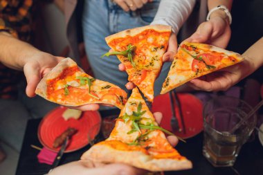 Yemek yemek. İnsanların ellerinin biberli pizzadan dilimler aldığı yakın çekim. Arkadaş gurubu pizzayı paylaşıyor. Fast food, arkadaşlık, eğlence, yaşam tarzı..