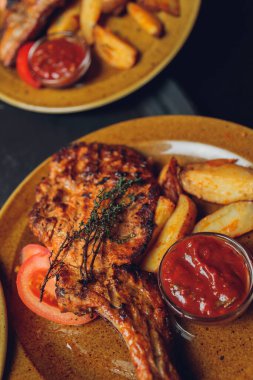 Masada ızgara kaburga bifteği ve sarı patates dilimleri ve tabağın üstündeki tabakta yağ ile fotokopi alanı..