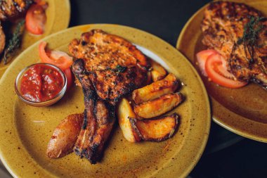 Masada ızgara kaburga bifteği ve sarı patates dilimleri ve tabağın üstündeki tabakta yağ ile fotokopi alanı..