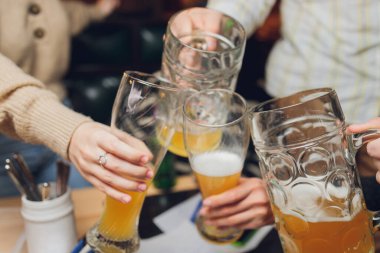 Bira bahçesinde bira bardağına yakın çekim yapan dört arkadaş..