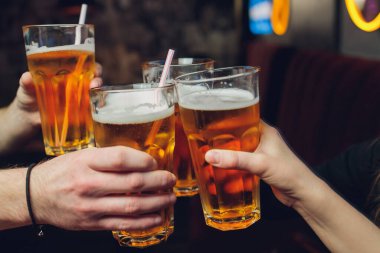 Bira bahçesinde bira bardağına yakın çekim yapan dört arkadaş..