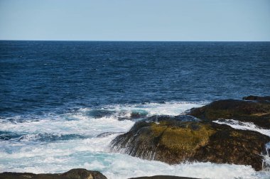 Küçük deniz dalgaları kıyıdaki taşlara çarpıyor. Parlak güneşli bir gün ve dalgaların beyaz köpüğü. Hava kirliliğinin çevresel bir etkisi olarak buzulların erimesi.