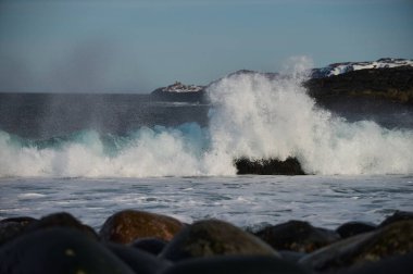 Küçük deniz dalgaları kıyıdaki taşlara çarpıyor. Parlak güneşli bir gün ve dalgaların beyaz köpüğü. Hava kirliliğinin çevresel bir etkisi olarak buzulların erimesi.