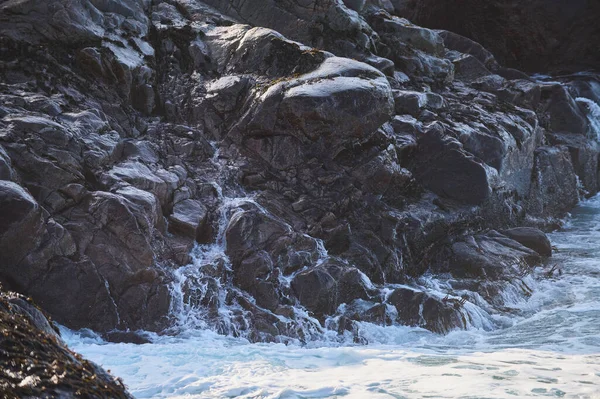 Small sea waves break against the stones of the shore. A bright sunny day and white foam of the waves. Melting glaciers as an environmental impact of air pollution.