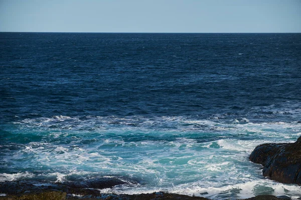 Piccole onde marine si infrangono contro le pietre della riva. Una giornata di sole luminoso e schiuma bianca delle onde. Sciogliere i ghiacciai come impatto ambientale dell'inquinamento atmosferico. — Foto Stock