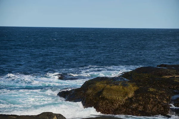 Невеликі морські хвилі розбиваються на камені берега. Яскравий сонячний день і біла піна хвиль. Танення льодовиків як екологічний вплив забруднення повітря . — стокове фото